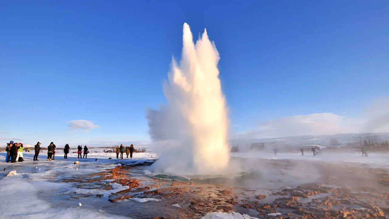 Erupting geysur, surrounded by rocks and ice. People stood watching