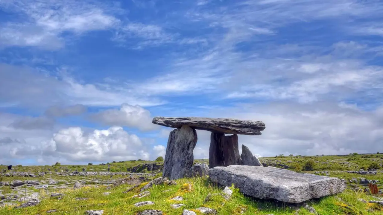 Rock tomb, with two vertical rocks and one horizontal rock on the top in a field, under a blue but cloudy sky