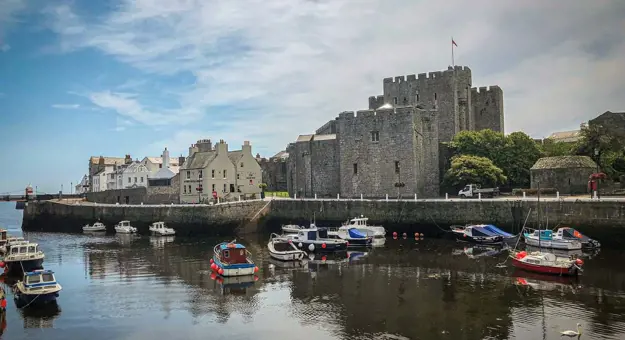 Castle Rushen from the water, with boats on the water and the buildings next to the castle nearer to the sea