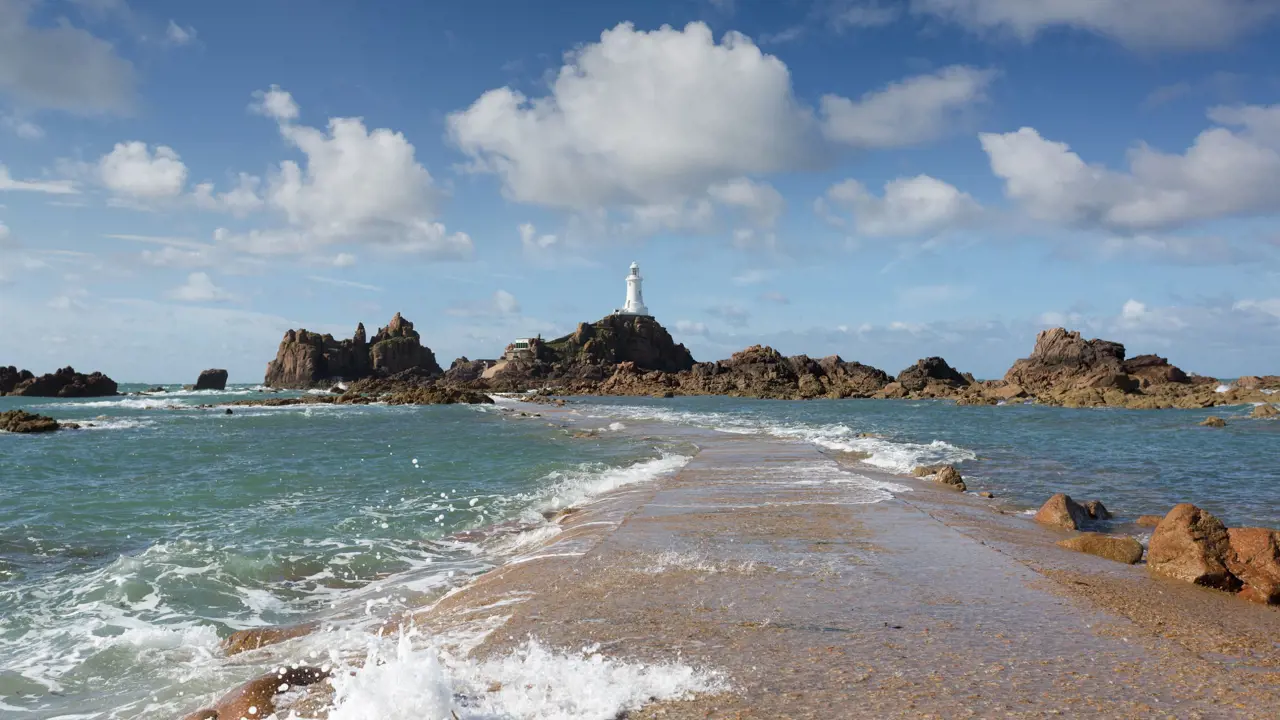 Long shot of the La Corbiere Causeway Light house, showing the sea below it, the rocks either side of it and a stone panel which runs towards it across the water