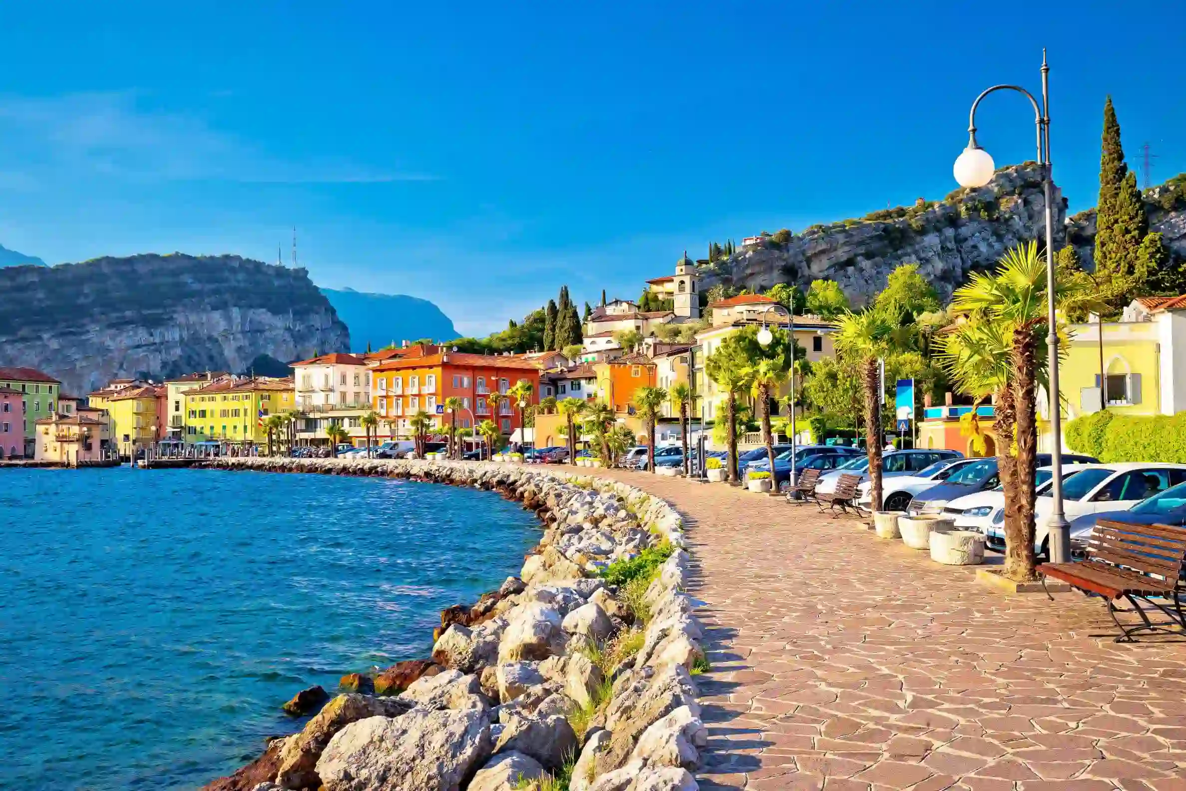 Waterfront in Torbole, Lake Garda, showing pavement and buildings and mountains in the distance